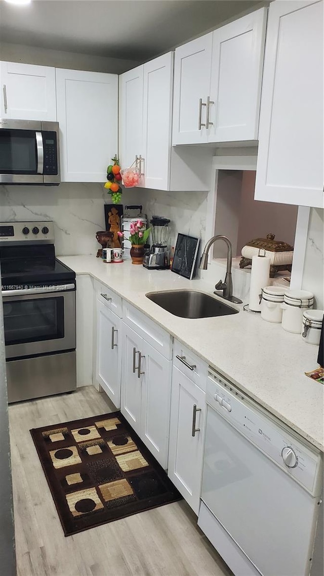 kitchen with white cabinets, sink, backsplash, appliances with stainless steel finishes, and light wood-type flooring