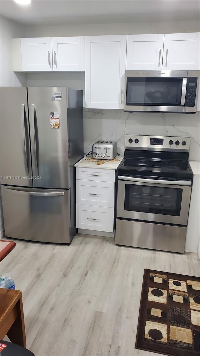 kitchen featuring appliances with stainless steel finishes, light wood-type flooring, white cabinetry, and decorative backsplash