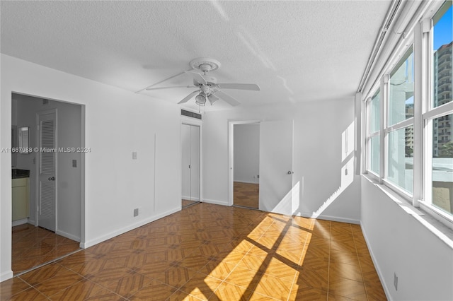 spare room with dark parquet flooring, ceiling fan, and a textured ceiling