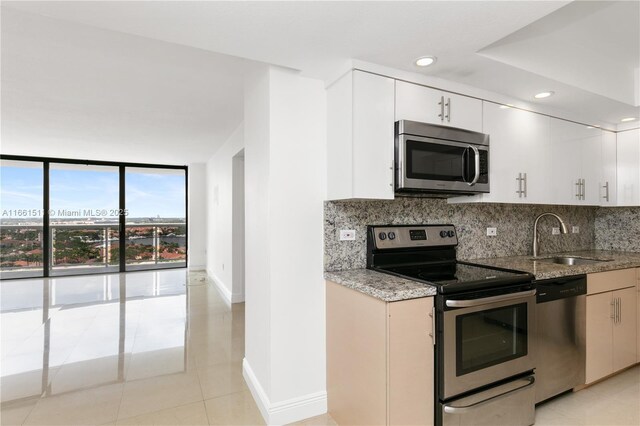 kitchen with sink, stainless steel appliances, white cabinets, expansive windows, and light tile patterned flooring