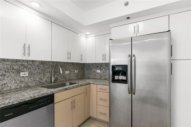 kitchen with backsplash, sink, light stone countertops, appliances with stainless steel finishes, and white cabinetry