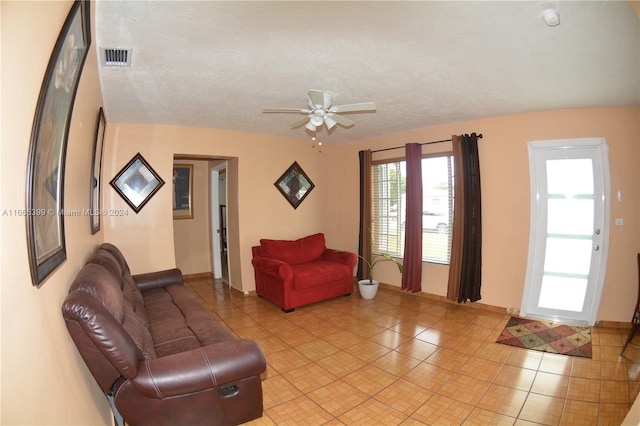 living room with ceiling fan, a textured ceiling, and light tile patterned flooring