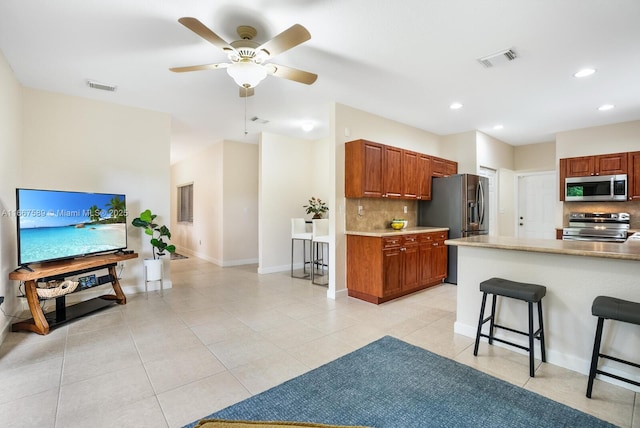 kitchen with ceiling fan, tasteful backsplash, a kitchen bar, light tile patterned floors, and appliances with stainless steel finishes