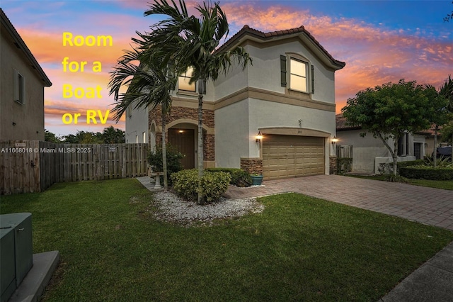 mediterranean / spanish house with decorative driveway, stucco siding, a front yard, a garage, and stone siding