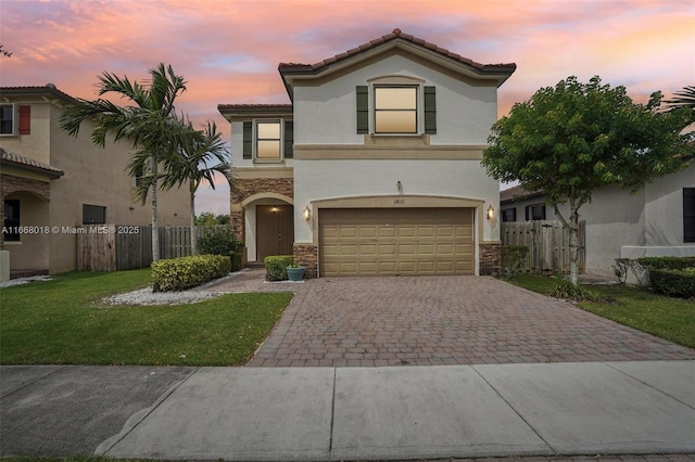 mediterranean / spanish-style house featuring stone siding, an attached garage, fence, decorative driveway, and stucco siding