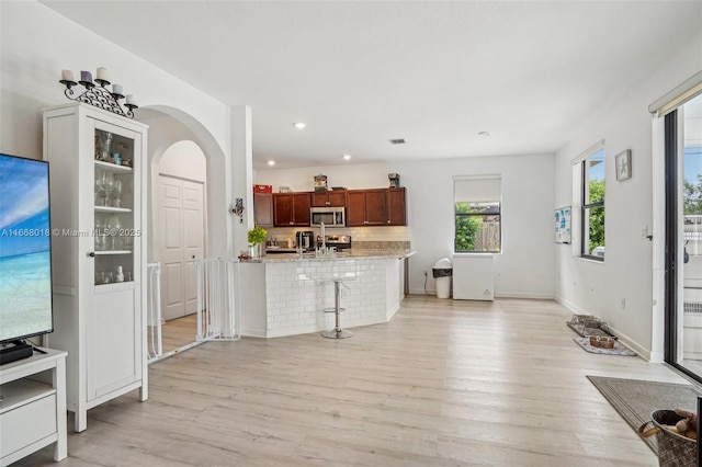 interior space featuring light wood-style flooring, a breakfast bar area, stainless steel appliances, and arched walkways