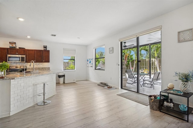 kitchen featuring visible vents, appliances with stainless steel finishes, a kitchen breakfast bar, light stone counters, and light wood-type flooring