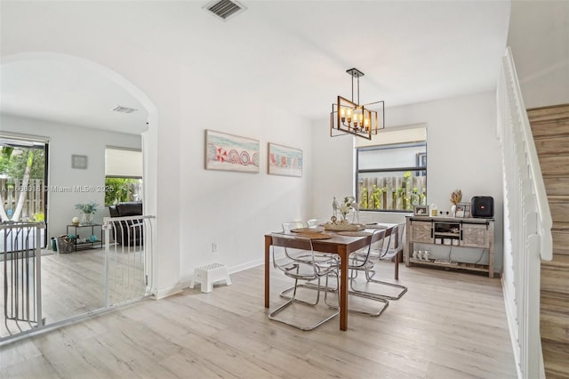 dining area featuring arched walkways, visible vents, an inviting chandelier, light wood-style floors, and baseboards