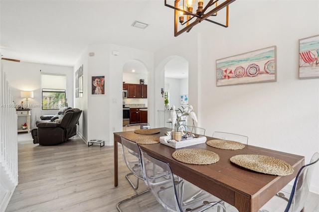 dining area with light wood-type flooring, an inviting chandelier, visible vents, and arched walkways