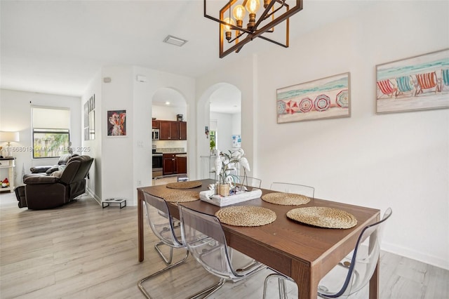 dining space featuring visible vents, arched walkways, light wood-style flooring, and baseboards