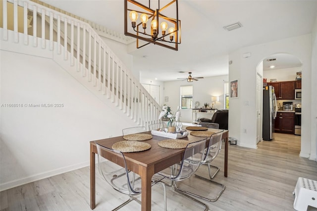 dining space with arched walkways, light wood-style flooring, baseboards, and stairs