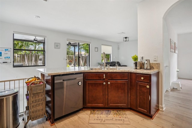 kitchen with arched walkways, a peninsula, a sink, light stone countertops, and dishwasher