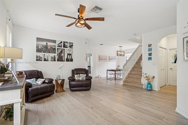 living area featuring ceiling fan with notable chandelier, light wood-style flooring, stairway, and visible vents