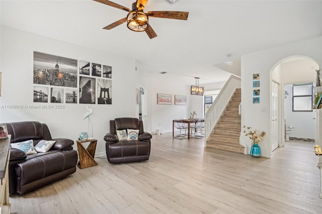 living area with arched walkways, stairway, light wood-style flooring, and a ceiling fan