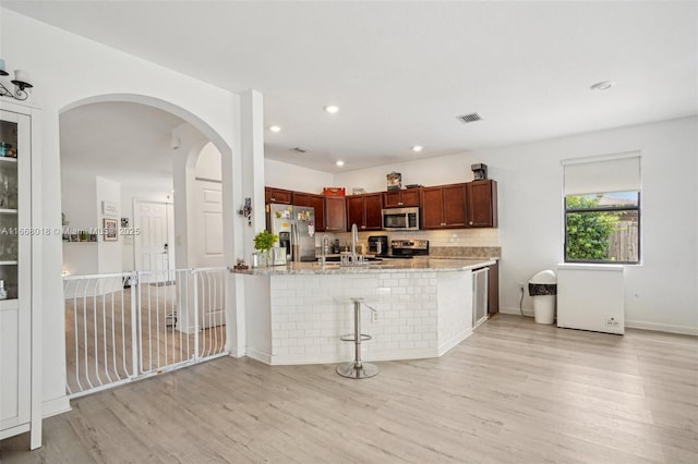 kitchen featuring light stone counters, visible vents, appliances with stainless steel finishes, light wood-type flooring, and a peninsula