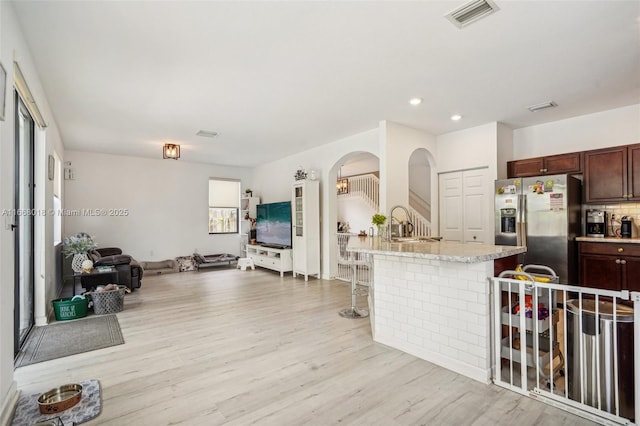 kitchen with light wood finished floors, a kitchen breakfast bar, open floor plan, a kitchen island with sink, and stainless steel refrigerator with ice dispenser