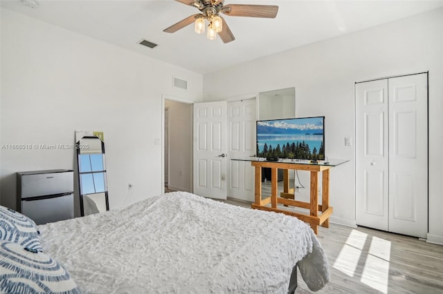 bedroom featuring light wood-type flooring, ceiling fan, visible vents, and two closets