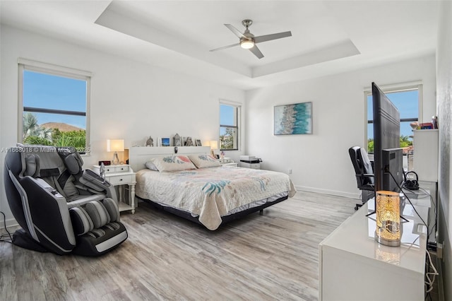 bedroom featuring a tray ceiling, multiple windows, light wood-style flooring, and baseboards