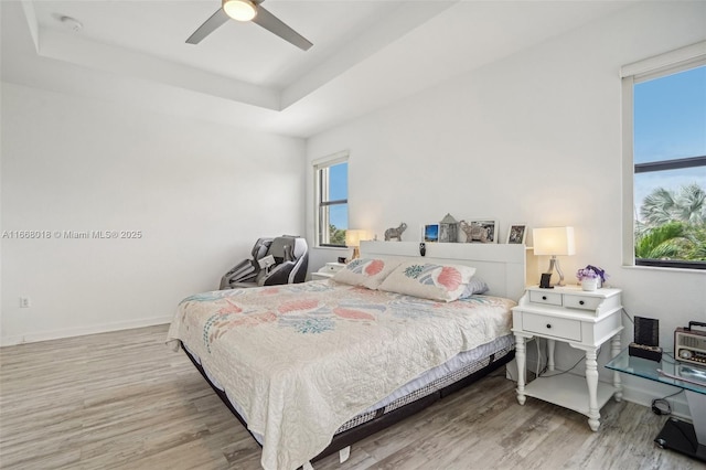 bedroom featuring light wood-type flooring, a raised ceiling, a ceiling fan, and baseboards