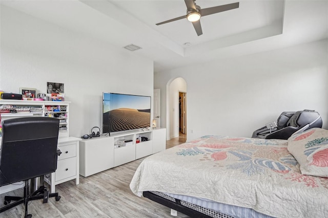 bedroom featuring visible vents, a raised ceiling, arched walkways, ceiling fan, and light wood-style floors