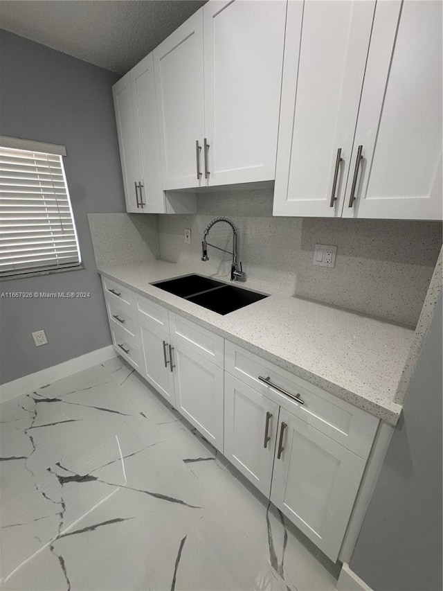 kitchen with white cabinetry, light stone counters, tasteful backsplash, and sink