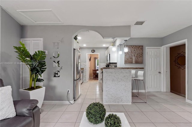 kitchen with white cabinetry, light tile patterned floors, pendant lighting, stainless steel appliances, and a kitchen bar