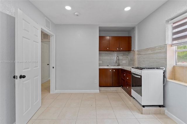 kitchen featuring backsplash, white gas range, light tile patterned floors, and sink