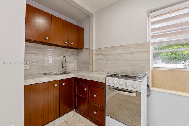 kitchen featuring light tile patterned flooring, sink, stainless steel range with gas cooktop, and decorative backsplash