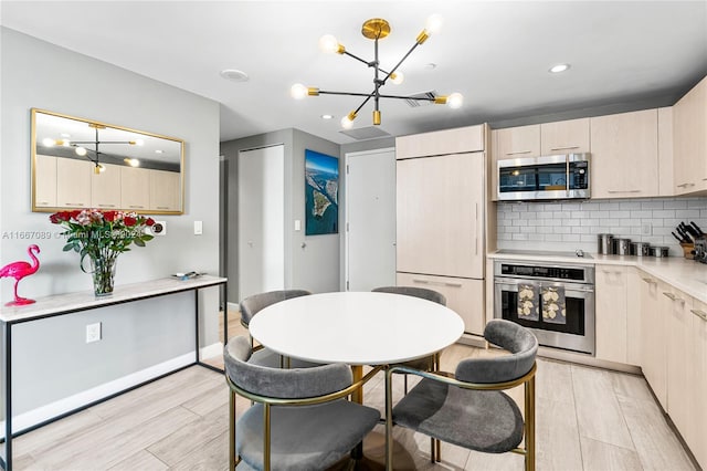 kitchen with pendant lighting, backsplash, a chandelier, stainless steel appliances, and light hardwood / wood-style floors