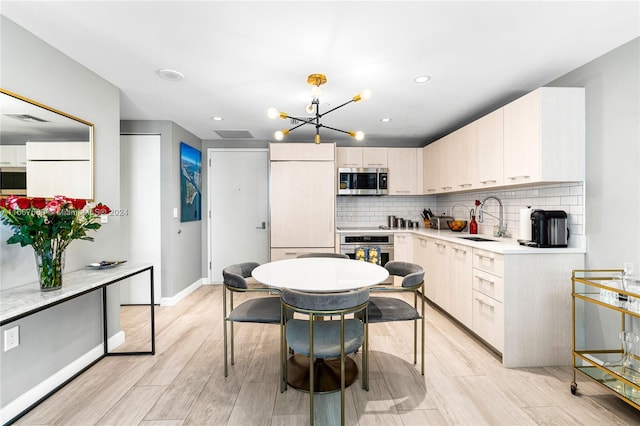 kitchen with light hardwood / wood-style floors, tasteful backsplash, sink, an inviting chandelier, and appliances with stainless steel finishes