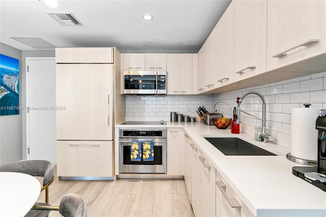 kitchen featuring appliances with stainless steel finishes, decorative backsplash, light hardwood / wood-style floors, and sink