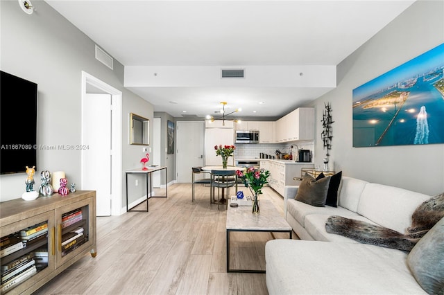 living room featuring sink, light hardwood / wood-style flooring, and a notable chandelier