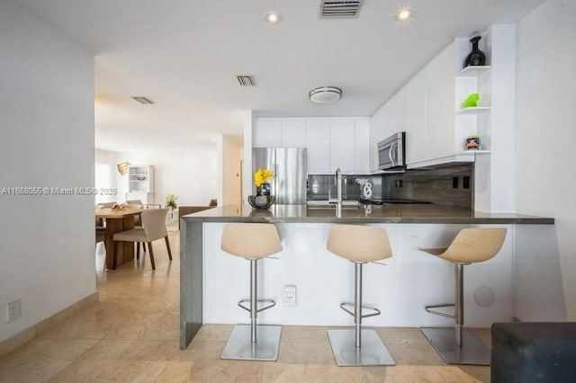 kitchen with open shelves, dark countertops, visible vents, appliances with stainless steel finishes, and a peninsula