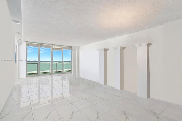 empty room with a water view, a textured ceiling, a wall of windows, and ornate columns