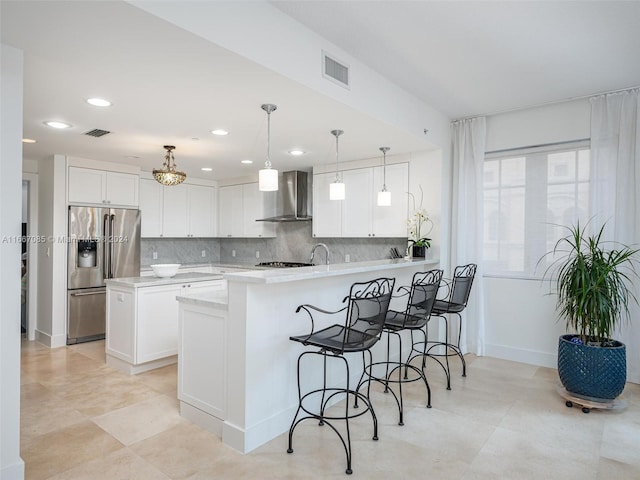 kitchen featuring pendant lighting, white cabinets, wall chimney exhaust hood, backsplash, and stainless steel fridge