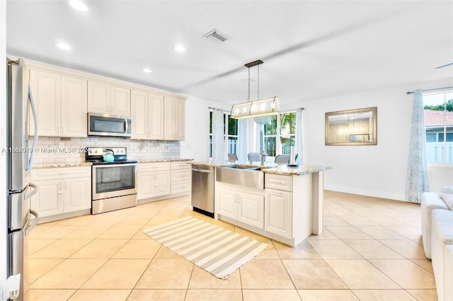 kitchen featuring hanging light fixtures, an island with sink, light stone countertops, sink, and stainless steel appliances