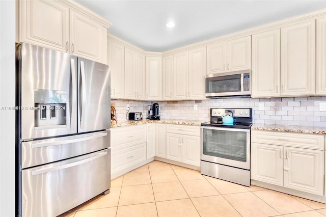 kitchen featuring cream cabinets, stainless steel appliances, backsplash, light tile patterned floors, and light stone counters