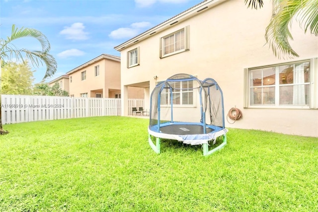 rear view of house featuring a yard and a trampoline