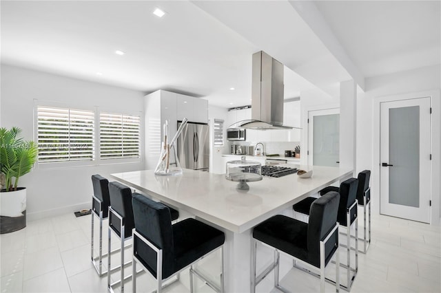 kitchen with white cabinets, appliances with stainless steel finishes, wall chimney range hood, and a breakfast bar area