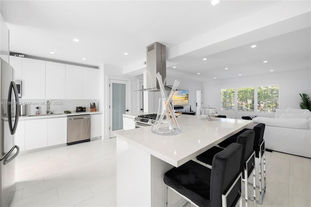 kitchen featuring stainless steel appliances, white cabinetry, island range hood, and a breakfast bar area