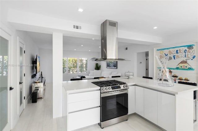 kitchen with kitchen peninsula, white cabinetry, island exhaust hood, and stainless steel range with gas cooktop