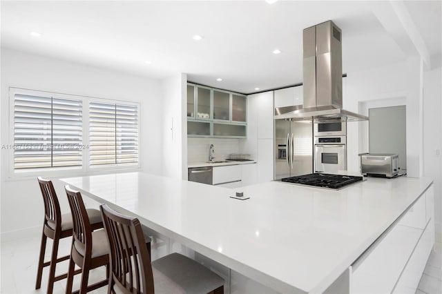 kitchen with island exhaust hood, stainless steel appliances, a breakfast bar, and white cabinetry