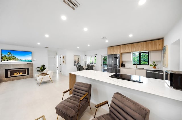 kitchen with a kitchen breakfast bar, light stone counters, a tiled fireplace, black appliances, and sink