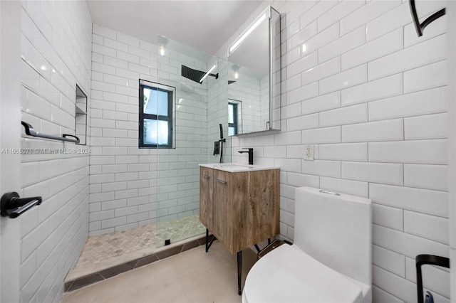 bathroom with tile walls, vanity, a tile shower, tile patterned flooring, and toilet