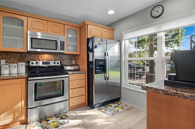 kitchen featuring dark stone countertops, backsplash, light hardwood / wood-style floors, and appliances with stainless steel finishes