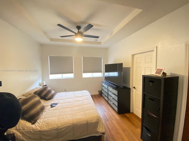 bedroom with ceiling fan, light wood-type flooring, and a tray ceiling