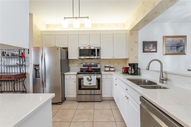 kitchen with appliances with stainless steel finishes, hanging light fixtures, white cabinetry, light stone counters, and sink