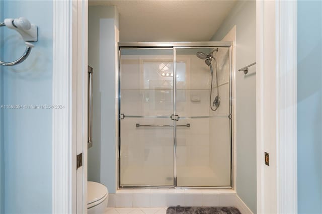 bathroom with a textured ceiling, a shower with door, toilet, and tile patterned floors