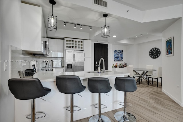 kitchen with hanging light fixtures, light hardwood / wood-style floors, white cabinets, stainless steel refrigerator with ice dispenser, and sink