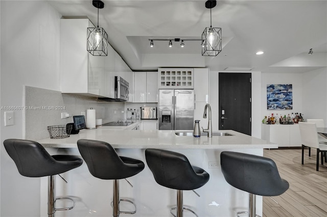 kitchen with hanging light fixtures, kitchen peninsula, white cabinetry, appliances with stainless steel finishes, and light hardwood / wood-style floors